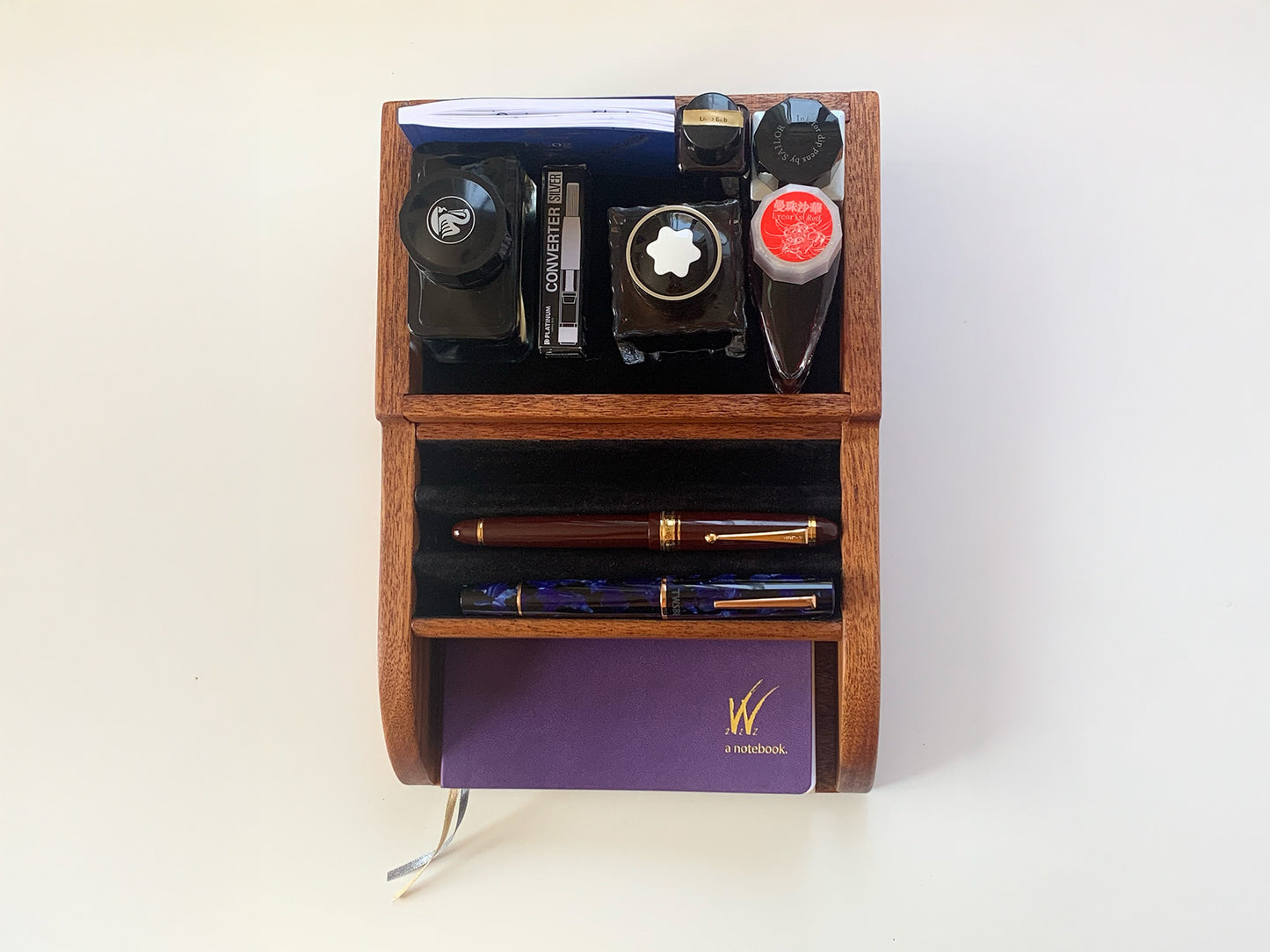 Top-down view of a handcrafted mahogany desktop organizer holding fountain pens, ink bottles, and notebooks