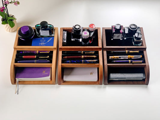 Top view of three Pen Tomo wooden desk organizers in cherry, mahogany, and walnut, neatly holding fountain pens, ink bottles, and notebooks
