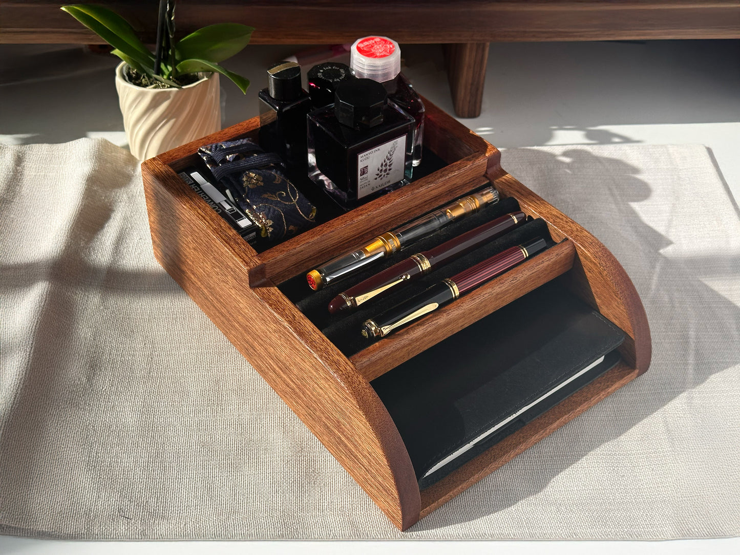 Front view of a handcrafted mahogany wood desktop organizer, Pen Tomo, neatly holding fountain pens, an ink bottle, and notepads