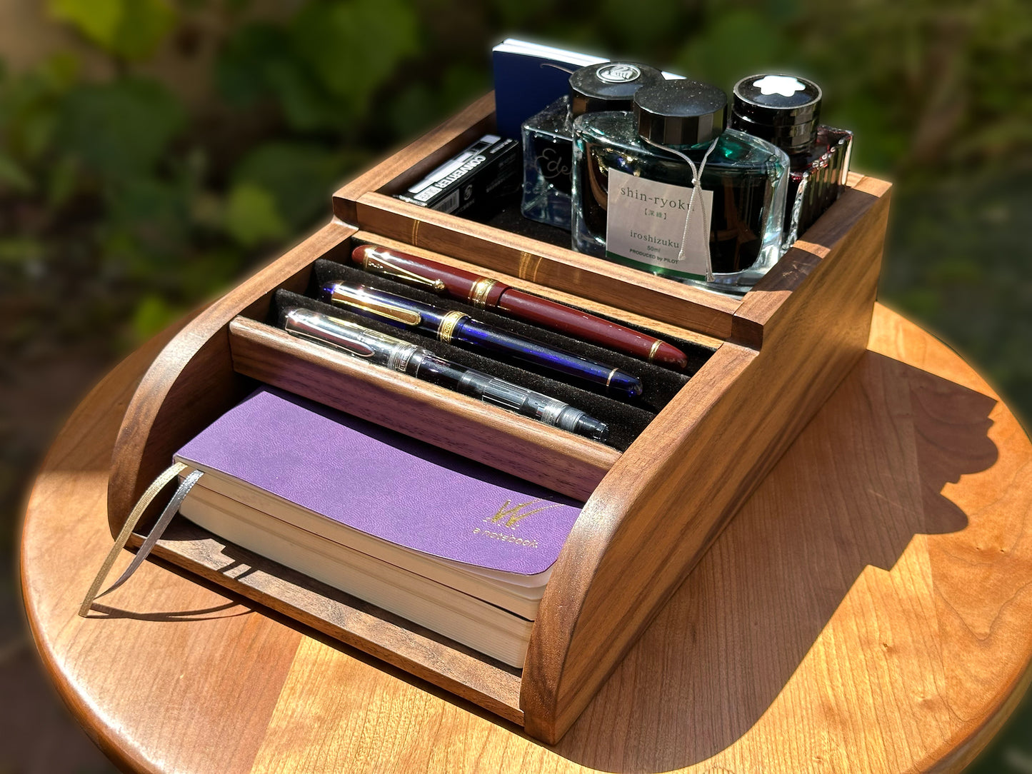 Pen Tomo - Walnut wood desk organizer with fountain pens, ink bottles, and a notebook on a wooden surface.