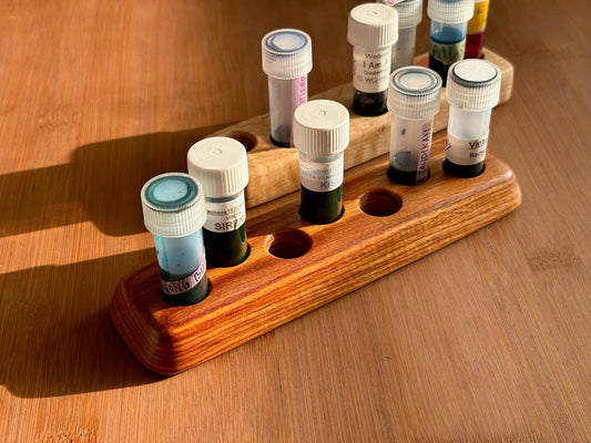 Handcrafted wooden ink sample vial holder with straight base and flared base, holding seven ink vials on a light wood desk